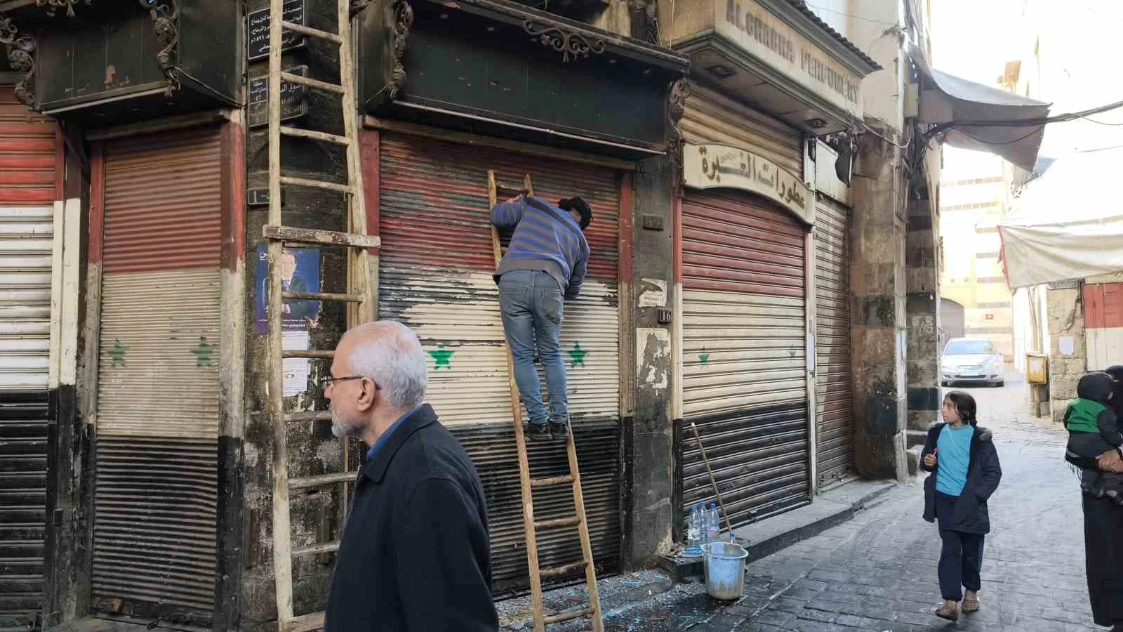 SURİYE’DEKİ HAMİDİYE ÇARŞISI’NDA ESNAF, KEPENKLERİN ÜZERİNDEKİ ESKİ SURİYE BAYRAĞINI KAZIMAYA